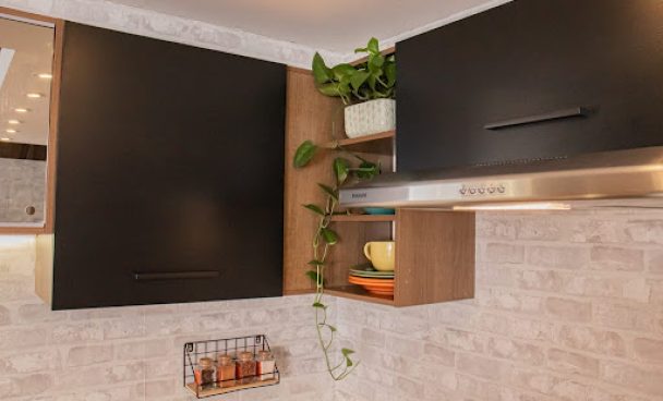 Armário aéreo da cozinha Agata, nas cores preto e rustic, com nichos decorados com plantas e louças.
