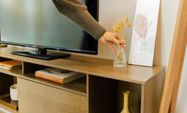 Rack em cores de madeira clara, com vaso de planta em cima, com televisão em cima e outros itens de decoração.