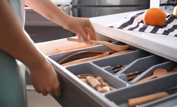 Pessoa abrindo uma gaveta de talheres e utensílios organizados em divisórias, uma excelente dica para ter uma cozinha funcional.