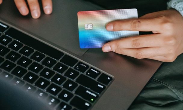 Pessoa segurando cartão de crédito em frente ao notebook como exemplo de como economizar na Black Friday.