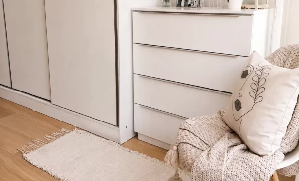Cômoda Madesa branca da linha Laura, com quatro gavetas, ao lado do guarda-roupa no quarto.