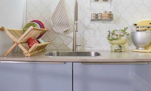 uma cozinha Lux cinza está alocada em uma cozinha com parede clara e detalhes em dourado. Sobre seu balcão estão uma batedeira, um vaso com suculentas e um escorredor de louças.