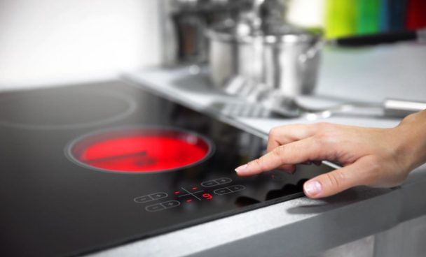 Uma superfície de fogão elétrico com uma mão ajustando o controle de temperatura, o painel do fogão com luz vermelha indicando funcionamento