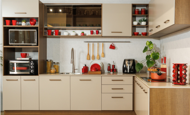 cozinha em L com armários de portas claras e detalhes em madeira. Utensílios com detalhes em vermelho dispostos sobre sua superfície e prateleiras.