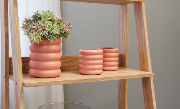 A imagem ilustra uma estante escada, na cor amadeirado claro, com vasos de cerâmica na decoração.