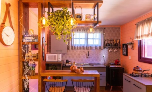 Cozinha Madesa, nas cores rustic e branco, com uma bancada e estante amadeirados e decorado com muitas plantas e cerâmicas.