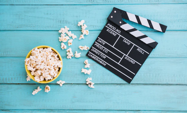 A imagem ilustra uma claquete e um balde pipoca sobre um fundo azul.