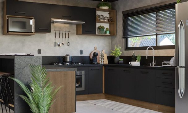 Cozinha moderna com armários pretos e detalhes em madeira. Ao fundo, uma bancada com fogão, micro-ondas e utensílios de cozinha. Plantas decorativas estão dispostas sobre a bancada e em um vaso ao lado. A iluminação é suave, com janelas que permitem a entrada de luz natural. O chão é revestido com azulejos claros.