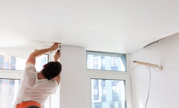 Pessoa em pé mexendo no teto de gesso, que está passando por manutenção