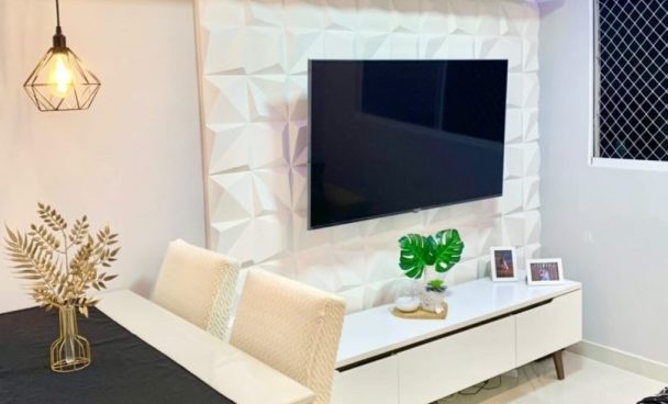 uma sala branca com detalhes geométricos em gesso na parede da televisão conta com uma mesa de jantar no mesmo ambiente. O Rack Madesa Reims Branco está embaixo da TV e, sobre ele, estão objetos decorativos e porta-retratos. A mesa tem uma toalha preta e um vaso com folhagens secas.
