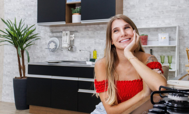 A imagem ilustra uma mulher loira de blusa vermelha no ombro na frente de uma cozinha planejada pequena, simples e barata.