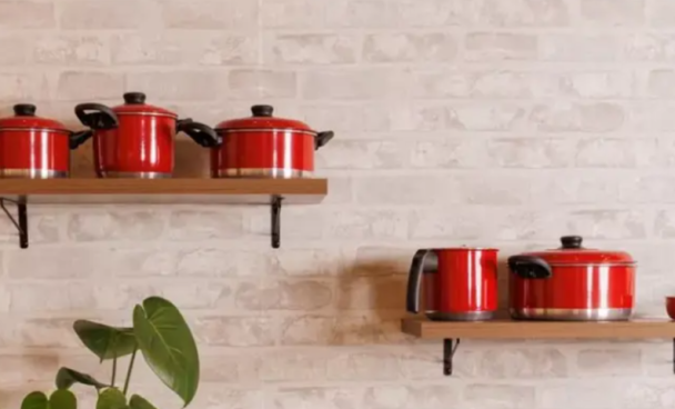 panelas vermelhas em diversos modelos estão dispostas sobre uma superfície escura em frente a um fundo branco, em conjunto com outros utensílios de cozinha