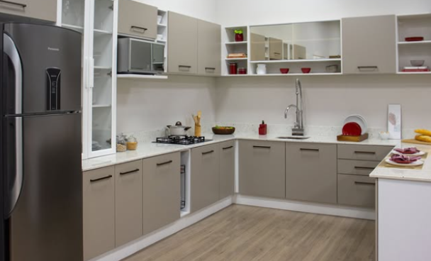 Cozinha completa com armários de canto na cor fendi, aéreos brancos com vidro, e uma geladeira grafite ao lado da bancada.