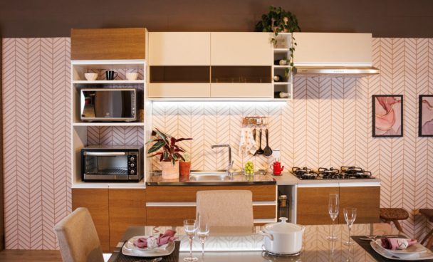 Cozinha decorada da linha Glamy Rustic, nas cores branco e crema. À frente dos módulos, há uma mesa de jantar posta.