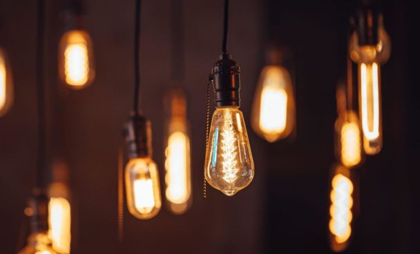 Várias lâmpadas de filamento estilo Edison penduradas, emitindo uma luz quente e amarelada em um ambiente escuro.