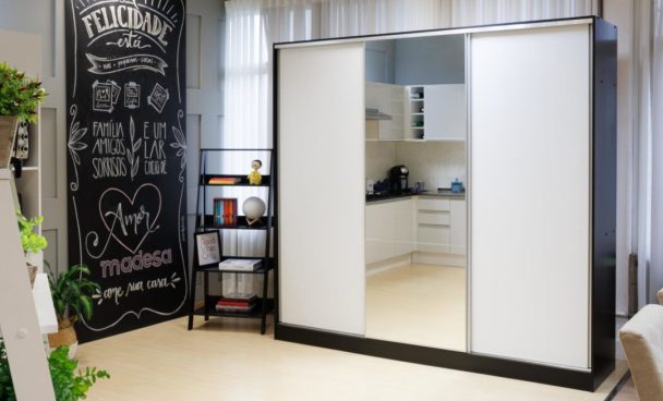 Guarda roupa de casal Royale Madesa, nas cores branco e preto. Ao lado, uma estante escada preta e um quadro com frases motivacionais e o slogan “Madesa, ame sua casa”.