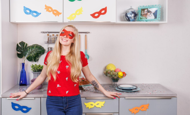 A imagem ilustra uma mulher loira em sua cozinha Madesa com uma decoração de festa tema carnaval.