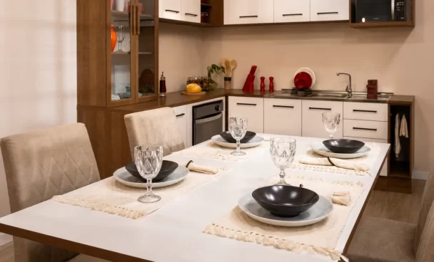 Mesa de jantar com cadeiras estofadas Madesa posta para quatro lugares, integrada à cozinha de um apartamento.