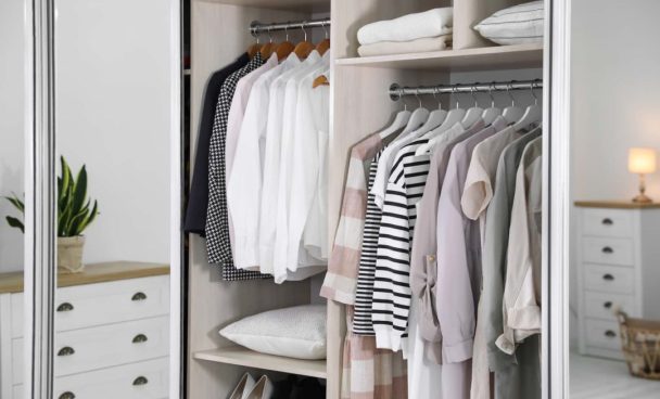 Camisetas e camisas penduradas dentro de um guarda-roupa organizado.