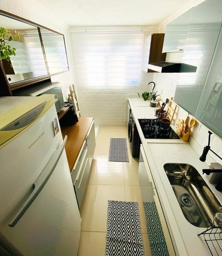 A imagem ilustra uma cozinha vista de cima com uma geladeira, armários e uma bancada com pia, representando as opções de presente para casa nova.