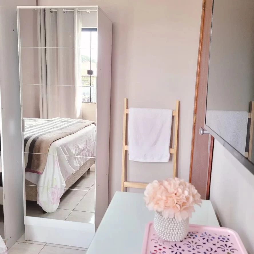 A imagem ilustra um quarto delicado, com uma sapateira branca espelhada como presente para casa nova.