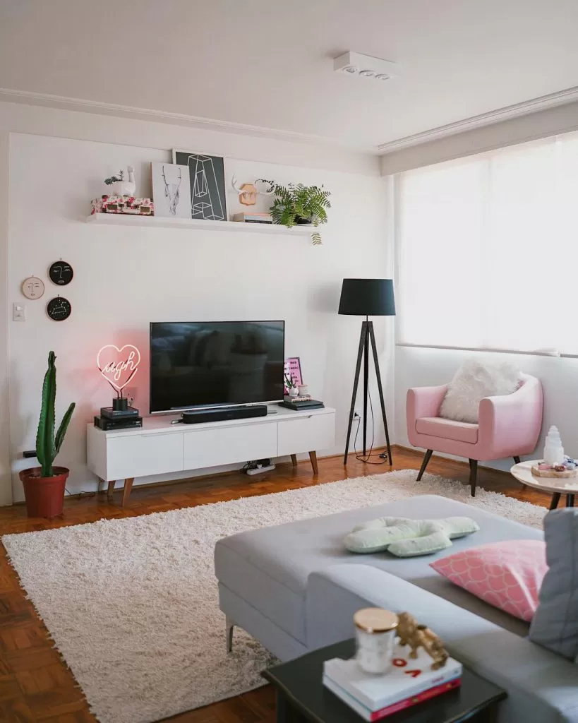 Sala de apartamento com paredes brancas e objetos cor de rosa como exemplo de como decorar um apartamento pequeno.