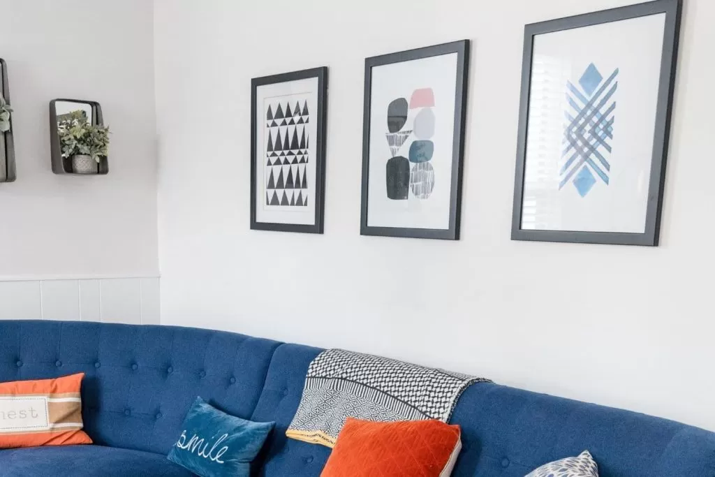 Sala de estar com sofá azul, almofadas coloridas e quadros pendurados na parede como exemplo de como decorar apartamento alugado.