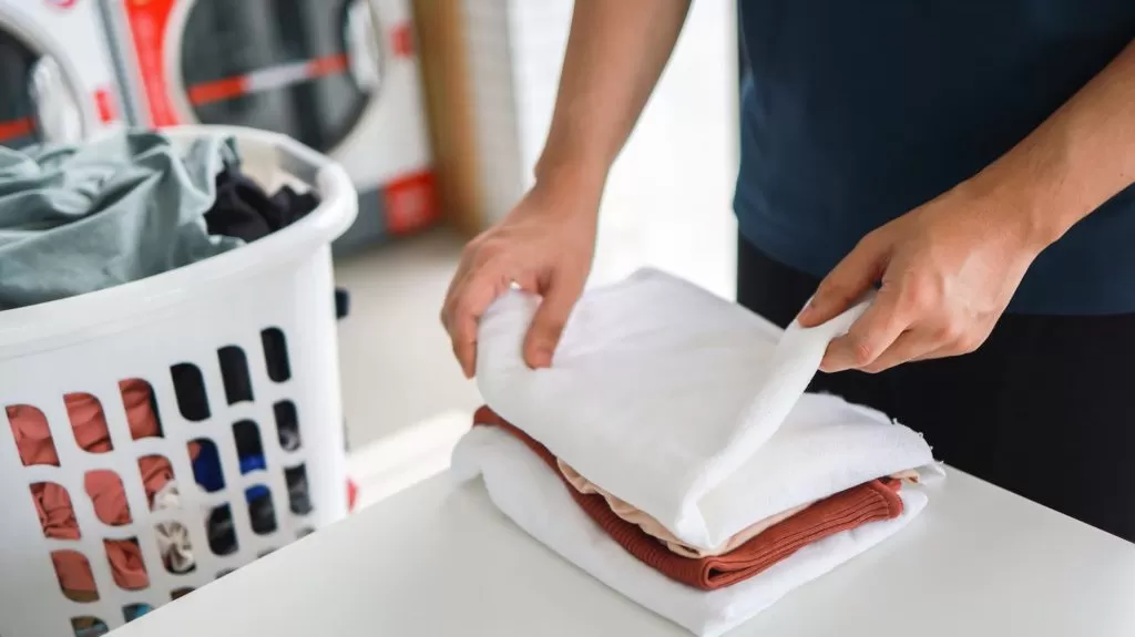 Pessoa dobrando roupas brancas e coloridas como exemplo de como organizar lavanderia.