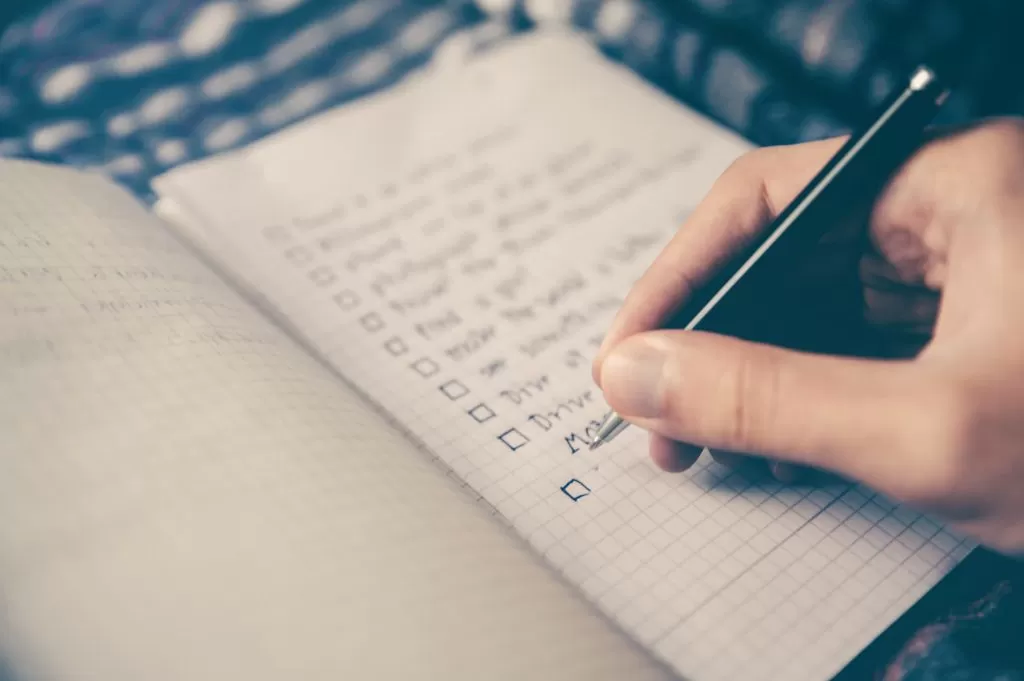 Pessoa escrevendo uma lista de tarefas em um caderno como exemplo de como organizar a rotina doméstica.