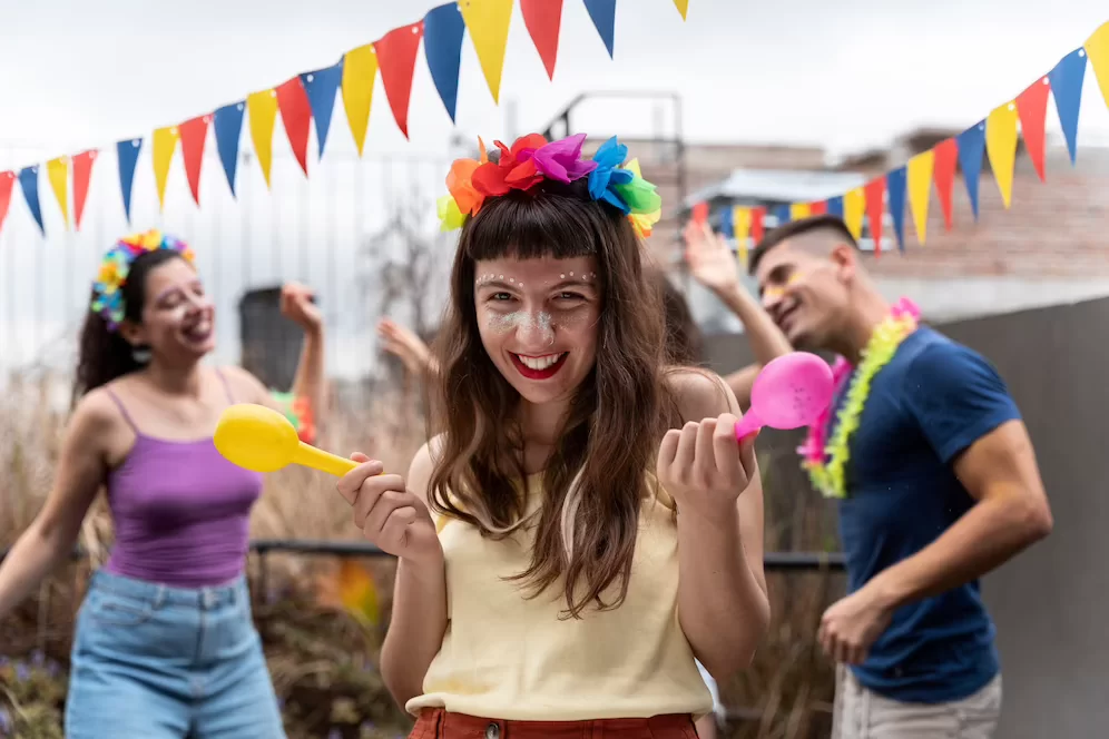A imagem ilustra uma mulher jovem com adereços coloridos de carnaval na cabeça, dando em sua festa tema carnaval no quintal.
