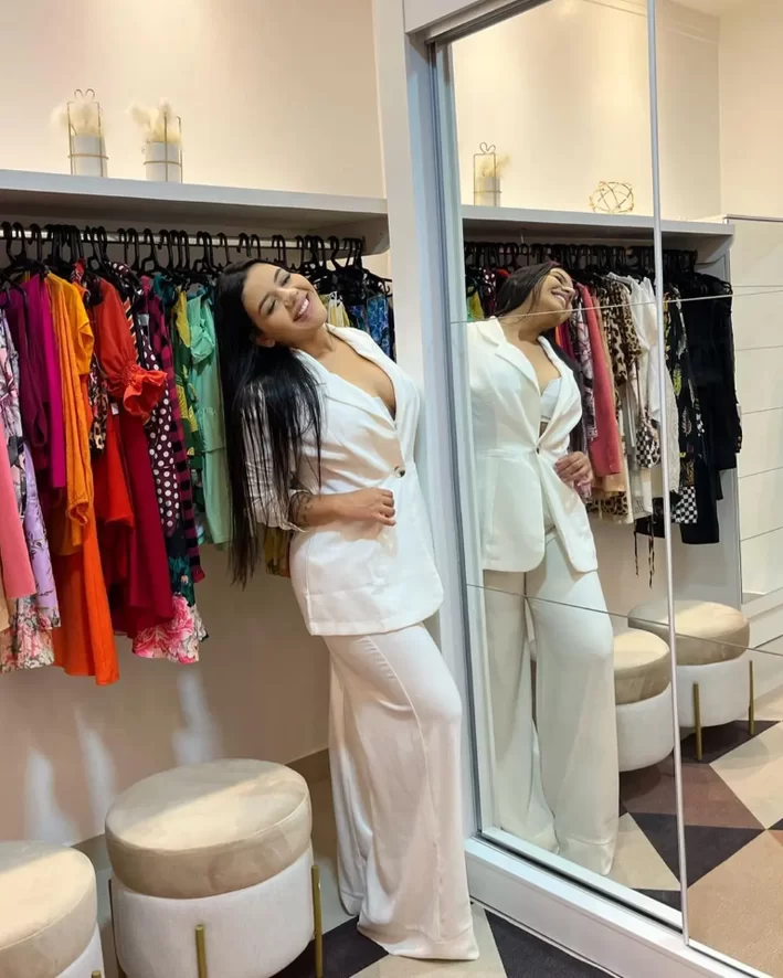 A imagem mostra uma cliente alta, morena e vestida com roupas brancas, em seu quarto com closet pequeno.
