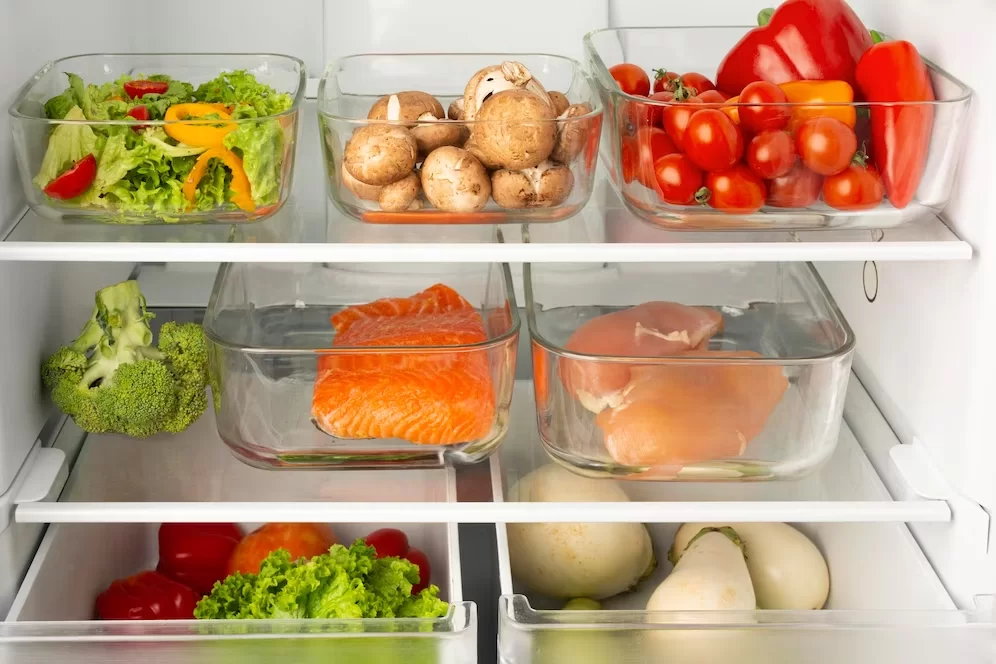 A imagem ilustra uma geladeira organizada por dentro, com potes de vidro e alimentos coloridos.