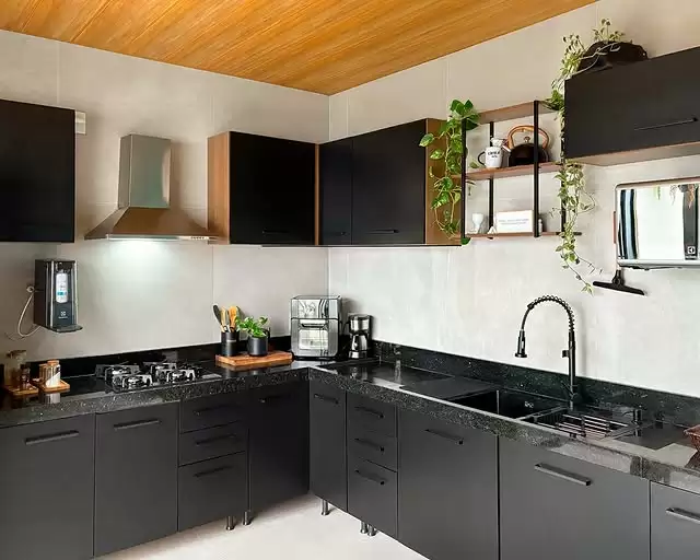 Cozinha com armários pretos e detalhes em madeira, pia com torneira preta, bancada de granito, prateleiras abertas com objetos decorativos e plantas, teto de madeira, e eletrodomésticos, incluindo micro-ondas e cafeteira.