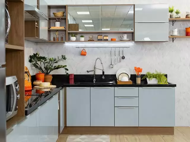 Cozinha com armários cinza-claro e detalhes em madeira, bancada preta, pia de aço inox, prateleiras abertas com utensílios e plantas, decorada com diversos objetos laranja.