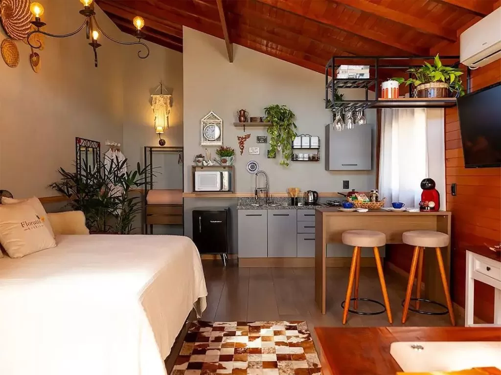 Sala de estar e cozinha americana Madesa ao fundo, com plantas, móveis amadeirados e estampas de decoração.