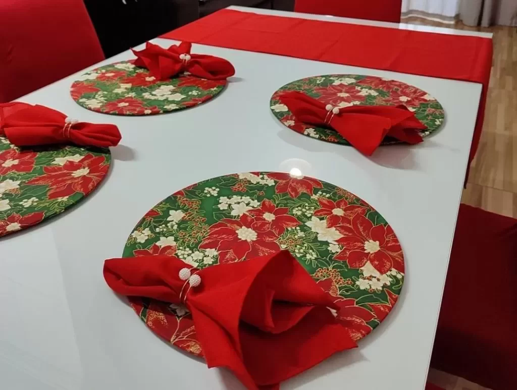 Mesa posta de Natal, com sousplat de estampas florais, toalha branca e guardanapos vermelhos.