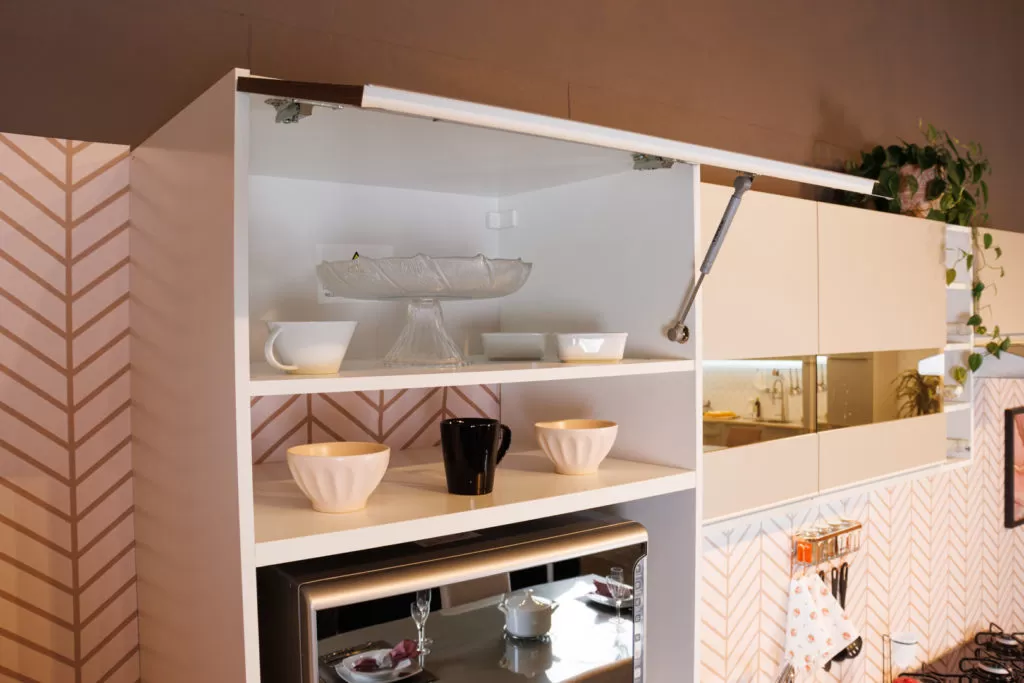 Armários aéreos de cozinha da linha Glamy, nas cores branco e Rustic, decorados com louças e eletrodomésticos.