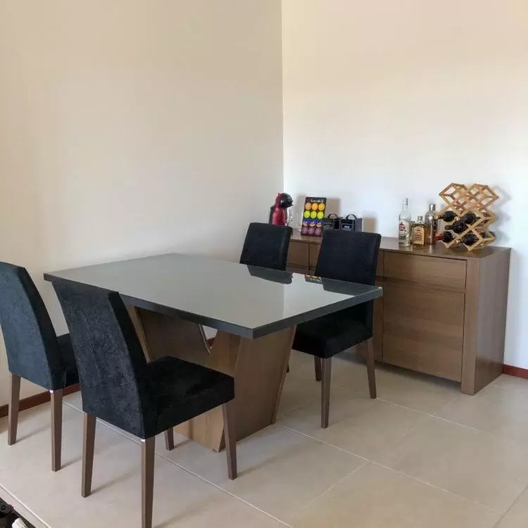 Sala de jantar composta por mesa retangular com tampo de madeira e aparador ao fundo com máquina de café e algumas bebidas em cima.