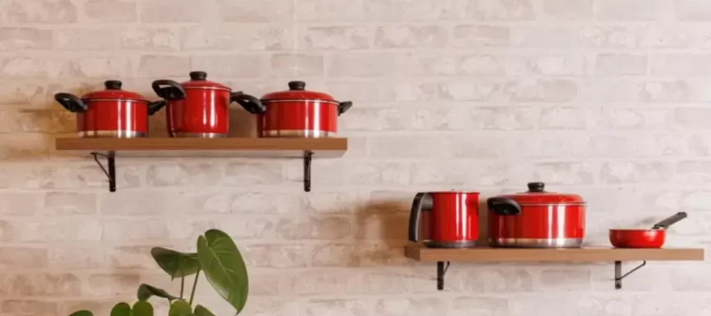 panelas vermelhas em diversos modelos estão dispostas sobre uma superfície escura em frente a um fundo branco, em conjunto com outros utensílios de cozinha