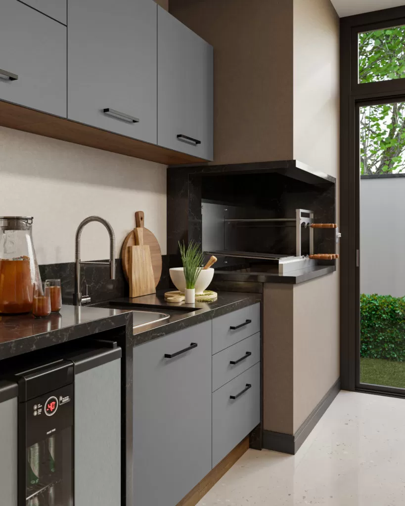 uma cozinha moderna com armários superiores em tom cinza e uma bancada escura. Um pia de inox está embutida na bancada, que também contém uma garrafa de vidro e utensílios de cozinha, como uma tábua de madeira. Ao lado, há um refrigerador embaixo da bancada. Uma grande janela permite a entrada de luz e mostra uma área verde do lado de fora.