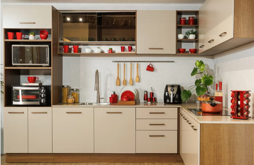 Armários de cozinha em tons claros com utensílios vermelhos e uma planta na bancada. Inclui micro-ondas e cafeteira.