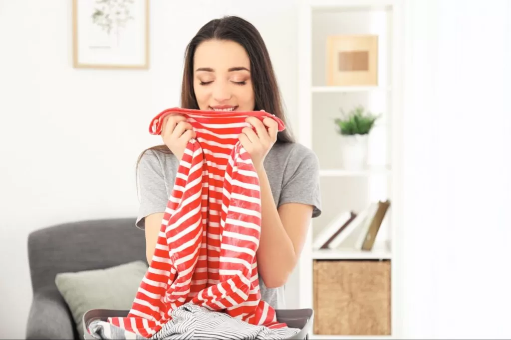 Mulher sorri enquanto segura uma camiseta listrada vermelha, dando um cheiro a ela em um ambiente aconchegante.