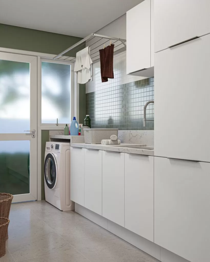 Lavanderia organizada, com roupas penduradas em varal, detergentes e cestos visíveis, e máquina de lavar ao fundo.