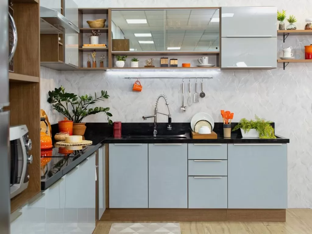 Cozinha moderna com armários cinzas, bancada de granito preto, pia de inox com torneira de cano alto, parede com revestimento branco texturizado, prateleiras de madeira com objetos decorativos, utensílios, plantas e louças na bancada.