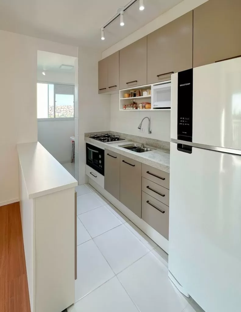 Cozinha moderna com armários brancos, iluminação embutida e decoração suave com plantas.