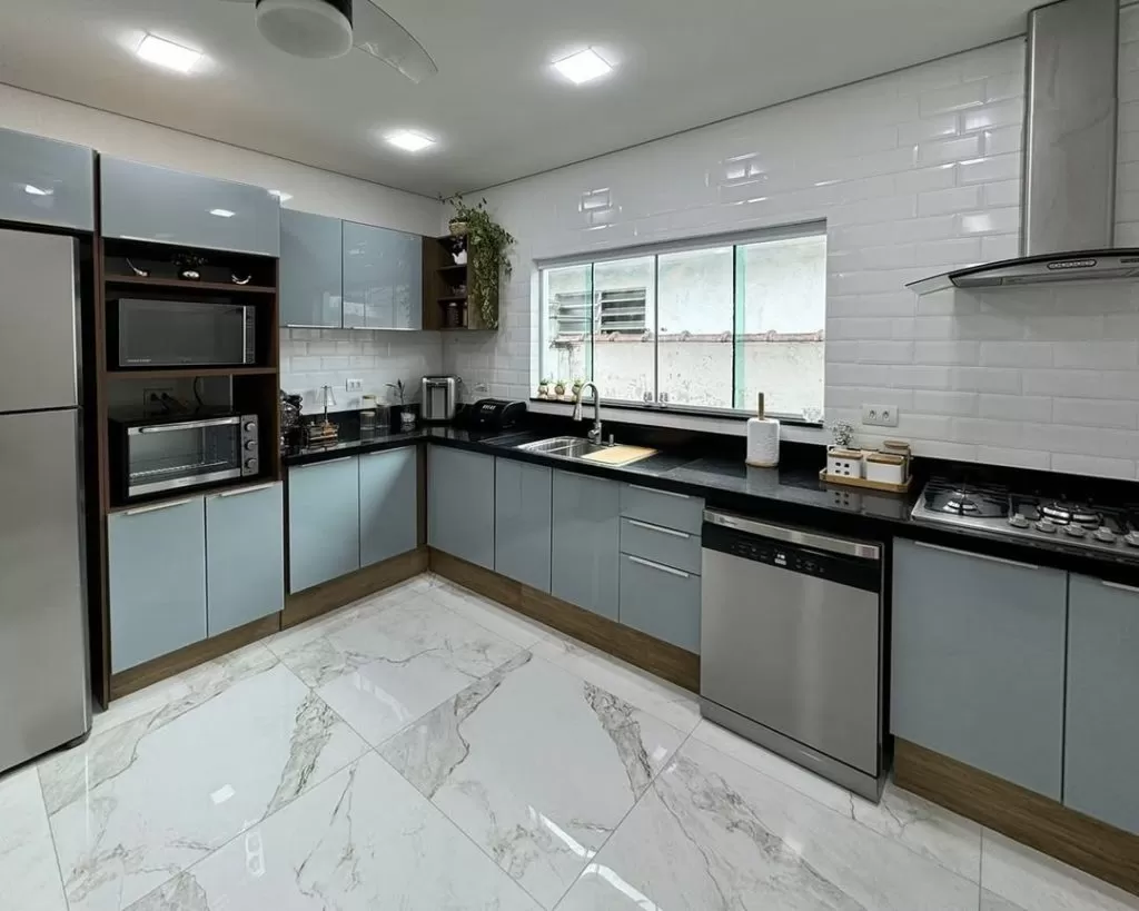 Cozinha moderna com armários cinza, utensílios de cozinha, plantas, e uma parede de azulejos brancos com padrão delicado.