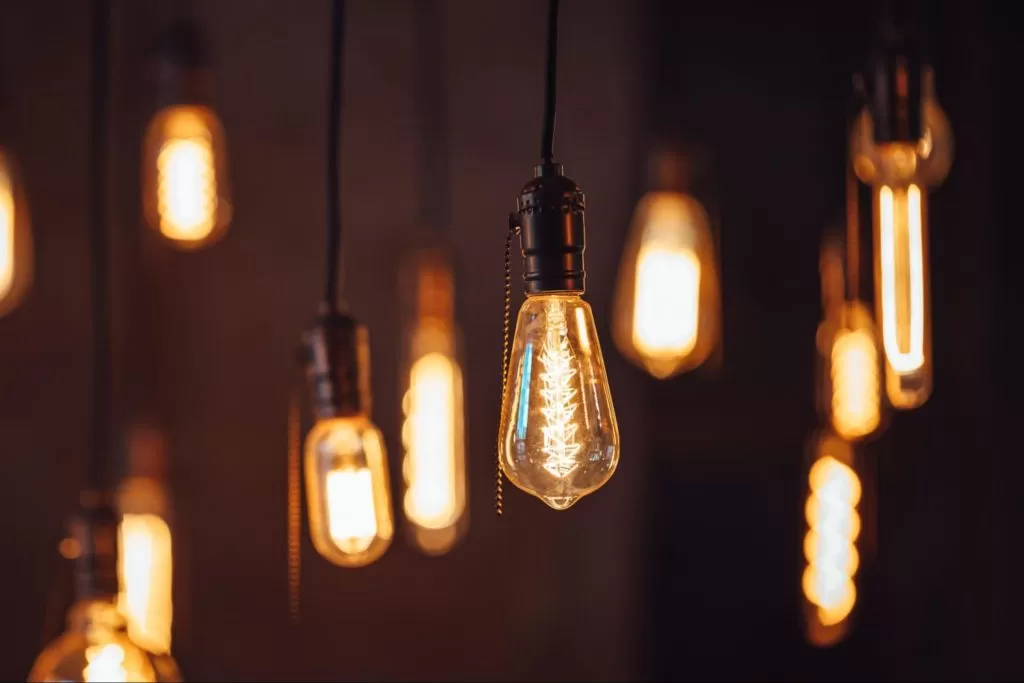 Várias lâmpadas de filamento estilo Edison penduradas, emitindo uma luz quente e amarelada em um ambiente escuro.