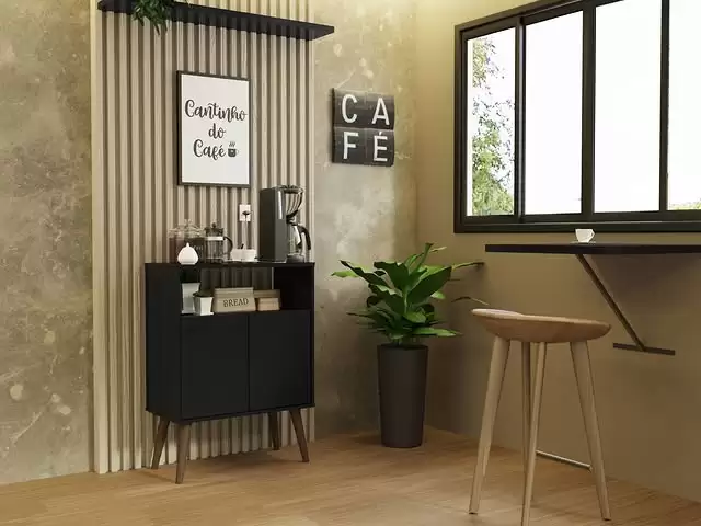 Cantinho de café decorado com uma parede de fundo com revestimento de ripas de madeira e uma parede de textura dourada, um móvel preto com máquina de café, xícaras e potes, uma placa com a frase "Cantinho do café", uma planta em vaso preto ao lado, uma janela grande com moldura preta e uma pequena mesa de madeira com um banquinho ao lado.