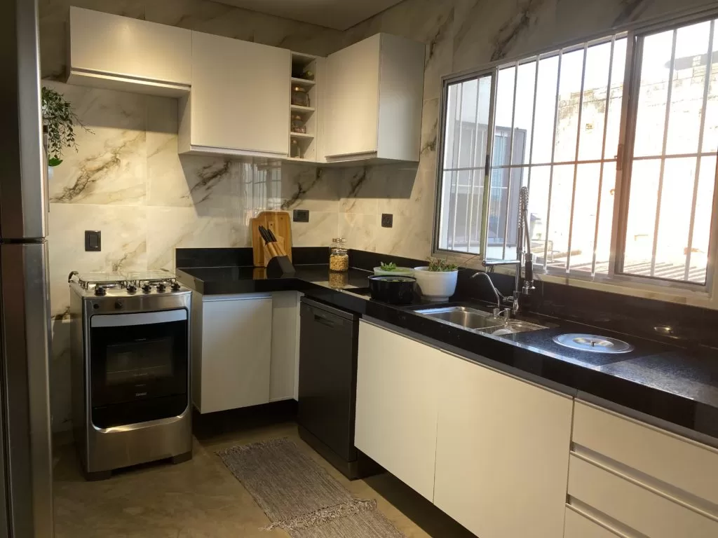 Pia em inox sobre bancada preta com portas brancas em frente a uma janela.