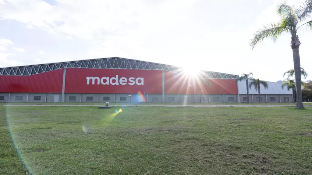 Fábrica vermelha Madesa com céu claro, a frente uma árvore e o gramado